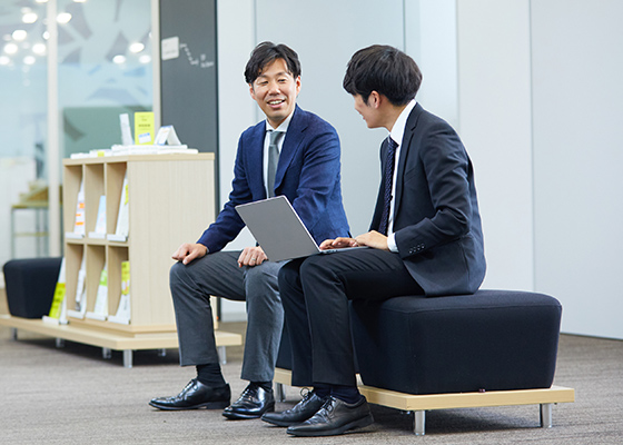 笑顔で同僚とコミュニケーションを取りながら仕事をする奈良 真史の写真