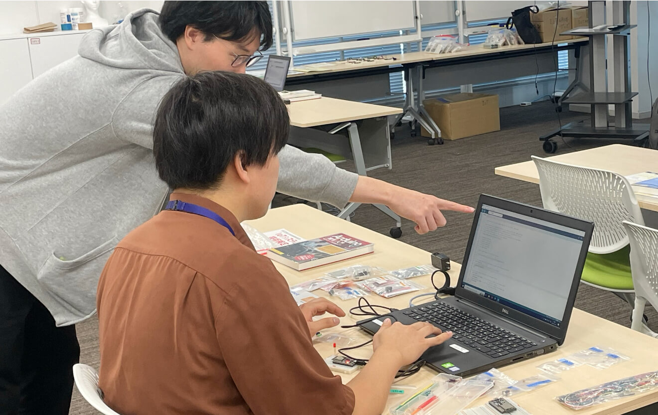 写真:PCを操作する受講生と、横でそのPCの画面を指さしながら指導を行っている道場講師の様子。