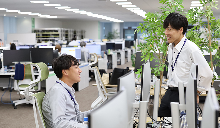 オフィス内の座席の写真。コミュニケーションをとっている2名の社員の様子。